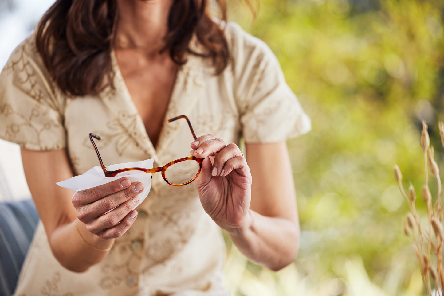 Woman holding eyeglasses cleaning them with a Zeiss Lens Wipe outdoors with a blurred natural background