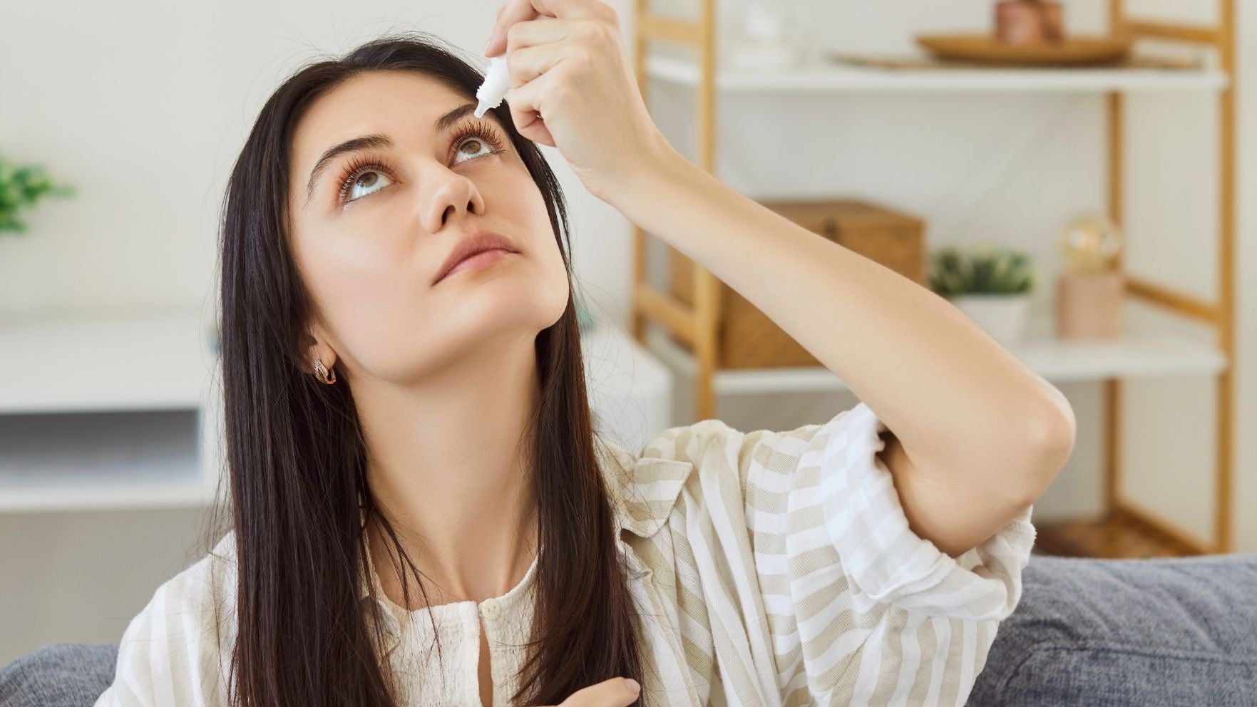Woman applying lubricating eye drops for dry eyes in a living room setting