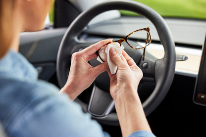 Person cleaning glasses with a Zeiss Lens Wipe inside a car.