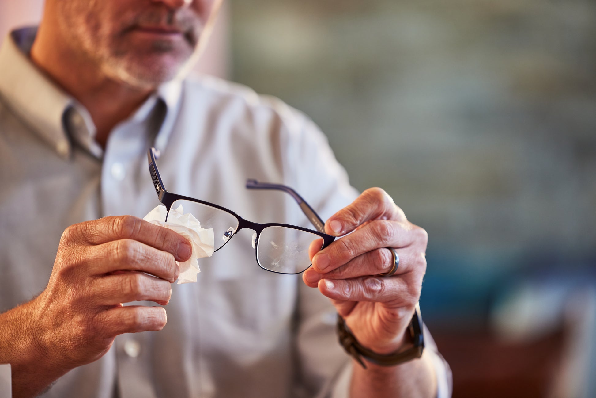 Man cleaning glasses with a Zeiss Lens Wipe against a blurred background