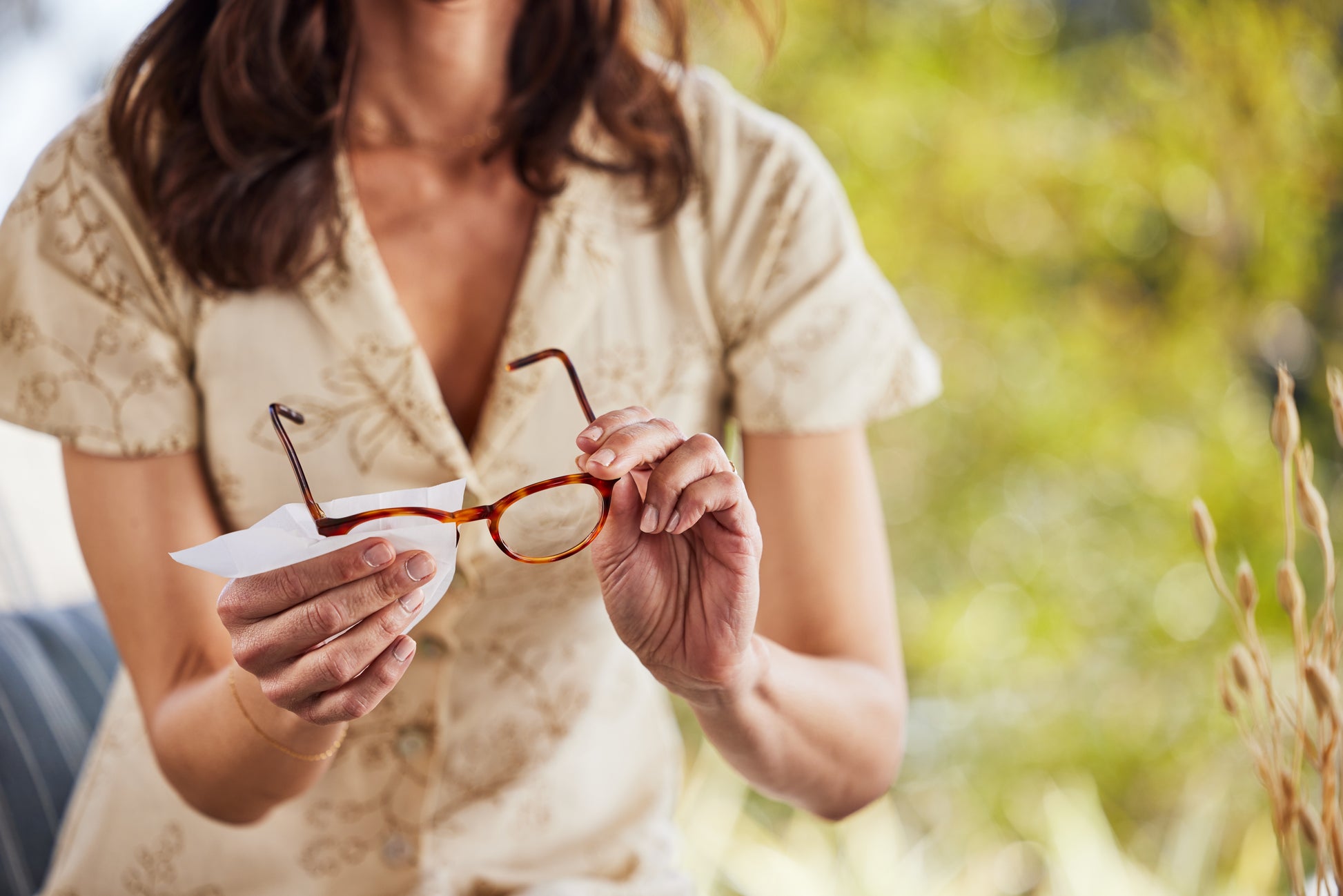 Woman holding eyeglasses cleaning them with a Zeiss Lens Wipe outdoors with a blurred natural background