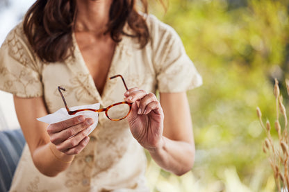 Woman holding eyeglasses cleaning them with a Zeiss Lens Wipe outdoors with a blurred natural background