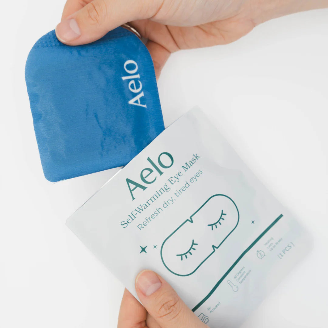 Aelo self-warming eye mask for dry eyes packaging on a white background with the mask being removed from the packaging