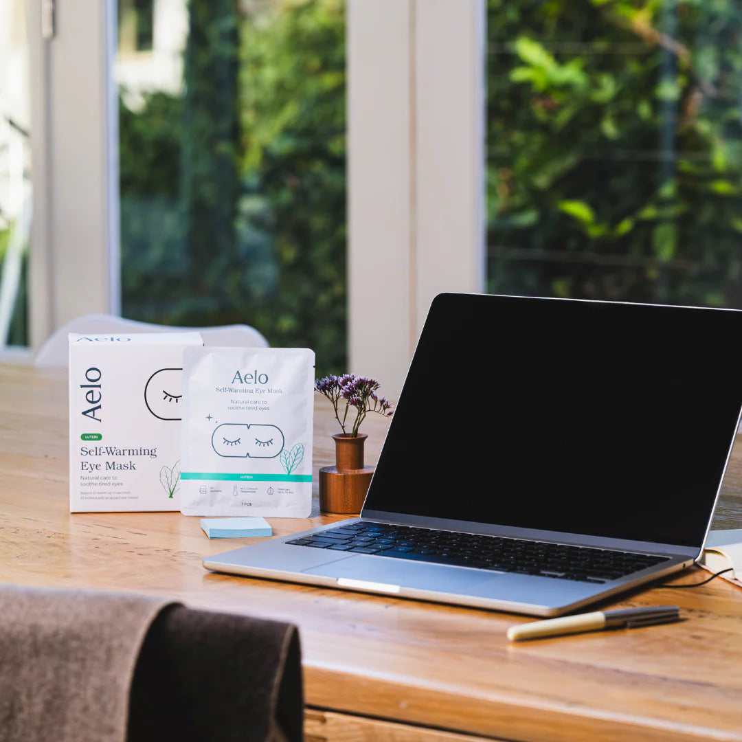 Laptop on a desk with Aelo self-warming eye mask packaging in the background