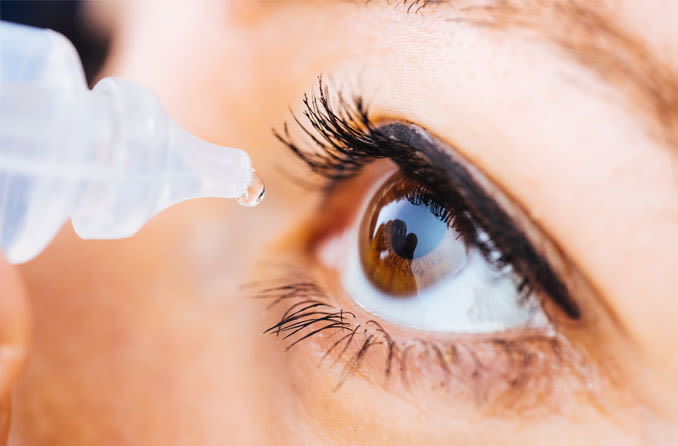 A close-up image of an eye receiving a drop from an eye dropper.